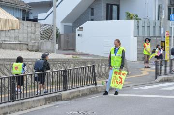 北玉小学校前で交通安全ボランティアをする女性米軍人とあいさつする子どもたちの写真